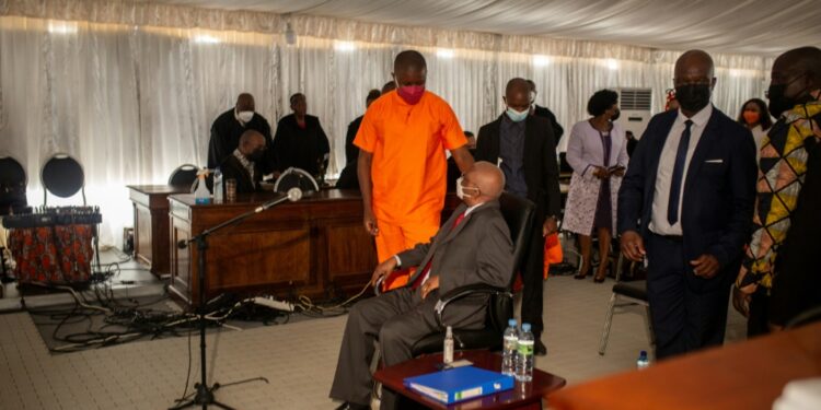 Mozambican Ex-President Defends Role At 'Hidden Debt' Trial Ex-President Guebuza, Seated, Talks To His Son Ndambi Guebuza, Wearing An Orange Prison Uniform. The Younger Guebuza Is A Defendant In The Long-Awaited Trial, Which Is Unfolding In A Marquee In A High-Security Jail | Afp